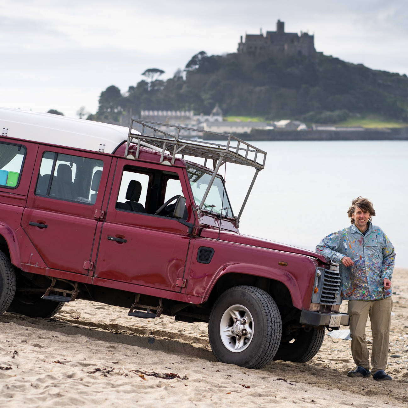 British & Cornish artist John Dyer at St Michael's Mount in Cornwall - pictured with his 2001 Dormobile 110 Land Rover parked on the beach at Marazion.