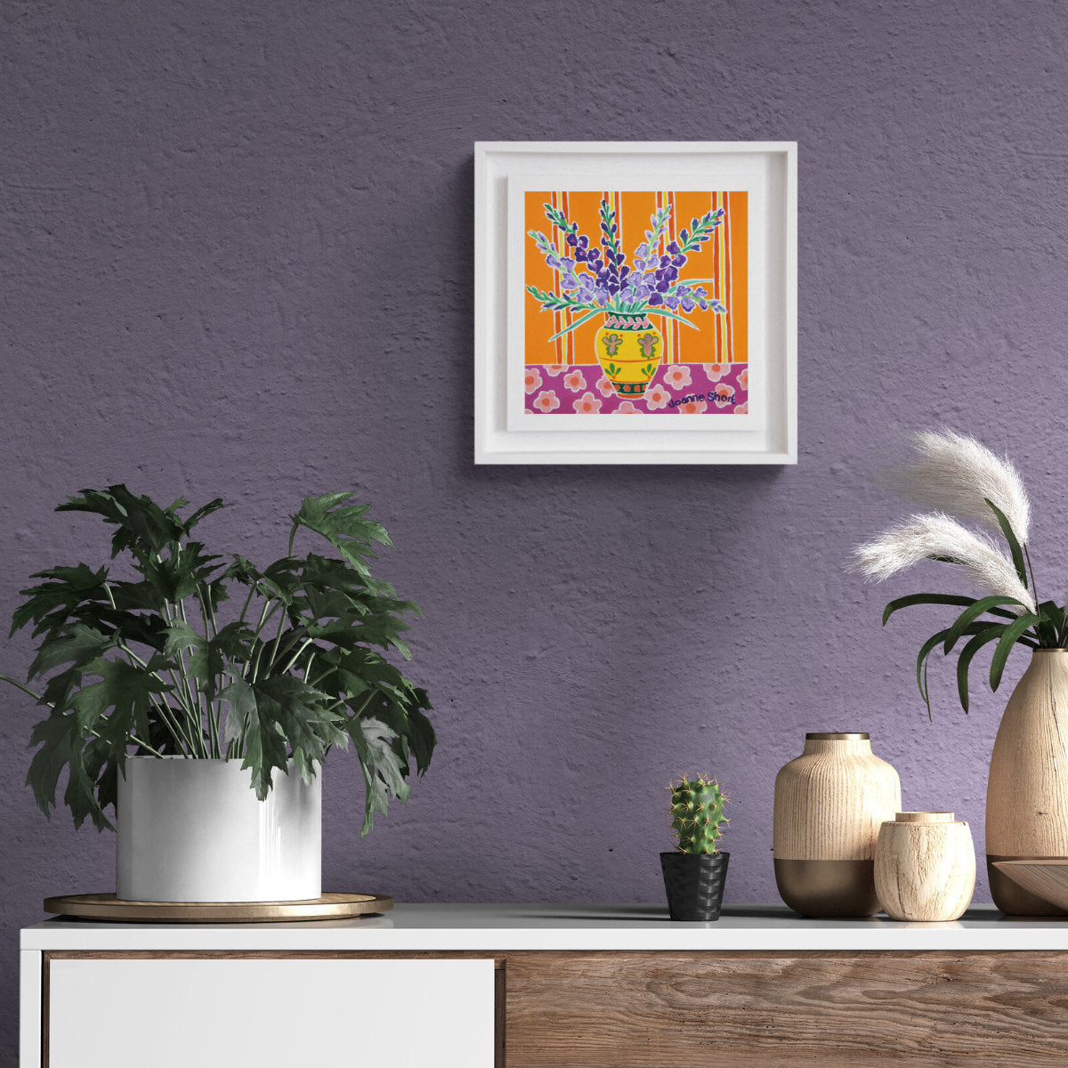 Framed artwork on a purple wall with decorative vases and plants below. 'Purple Gladioli in a Yellow Vase', 8 x 8 inches oil on canvas still life. Painting by Cornish Artist Joanne Short