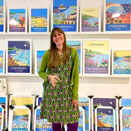 Cornish artist Joanne Short standing in front of her vintage style travel art posters of Cornwall