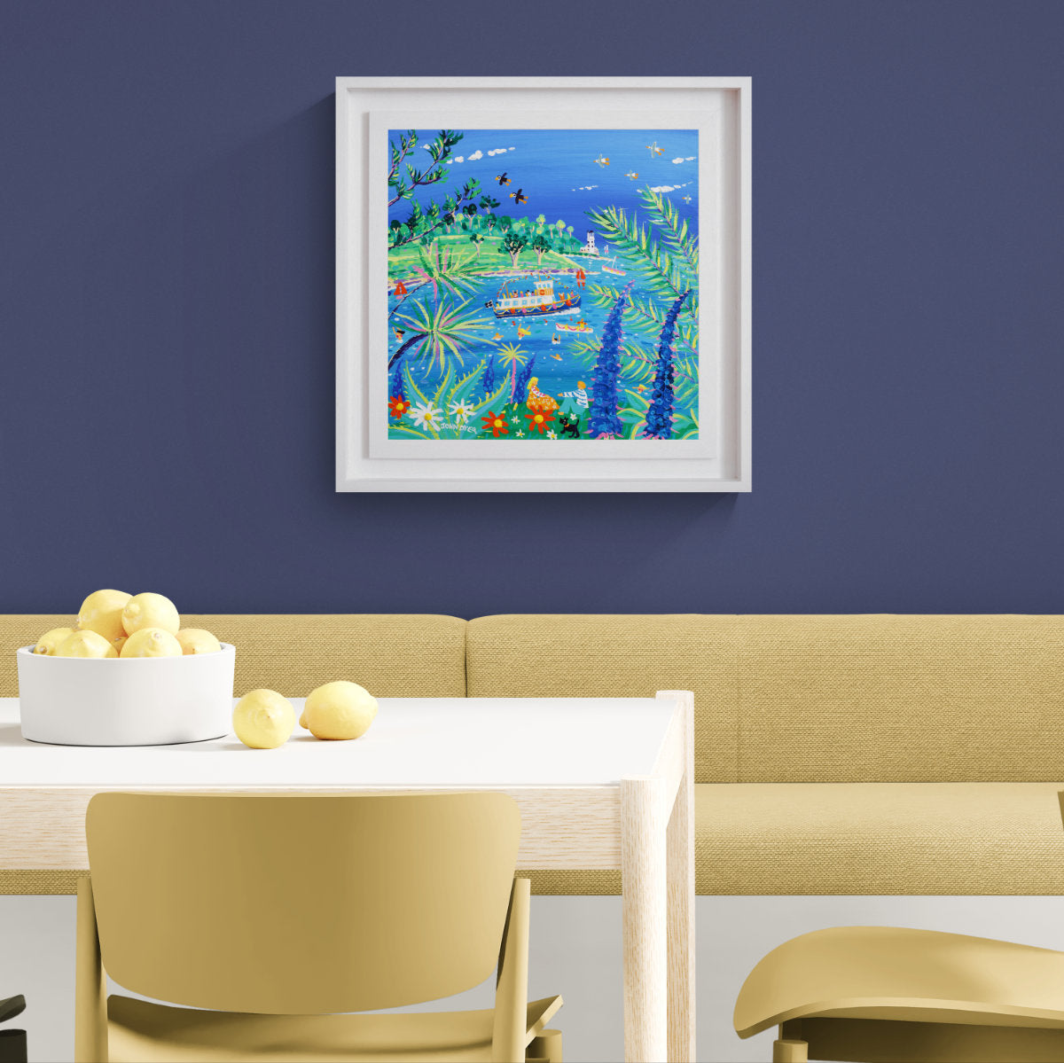 A framed colourful painting of an underwater scene hangs on a dark blue wall above a beige dining table and chairs with lemons in a bowl. 'Watching the Ferry go by, St Mawes’, 18 x 18 inches acrylic on canvas. Cornish Coastal Art. Painting by Artist John Dyer