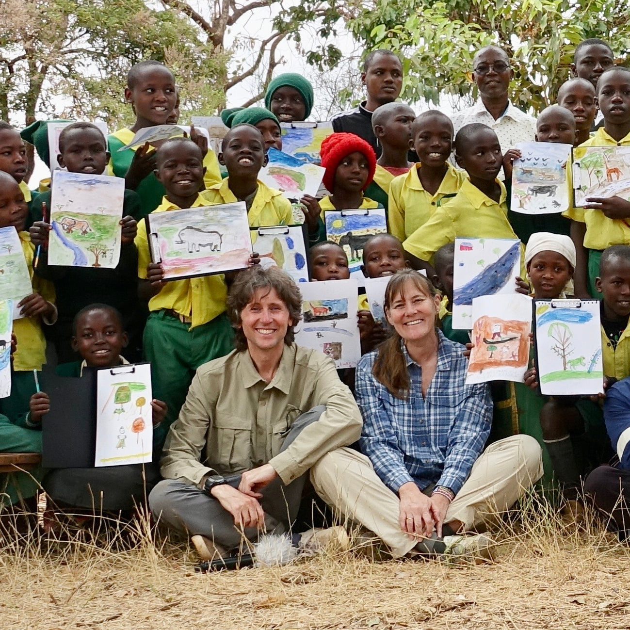 Kenyan school children proudly holding up their paintings of Africa from their Last Chance to Paint art workshop with British artists John Dyer and Joanne Short, who are seen in the foreground.