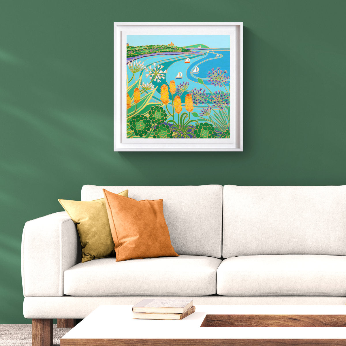 A framed colourful coastal seascape original painting hangs on a dark green wall above a white sofa with decorative pillows in a styled living room setting. Joanne Short Original Oil Painting of Cornwall. 'Castle Beach Summer, Falmouth'. 24 x 24 inches oil on canvas.