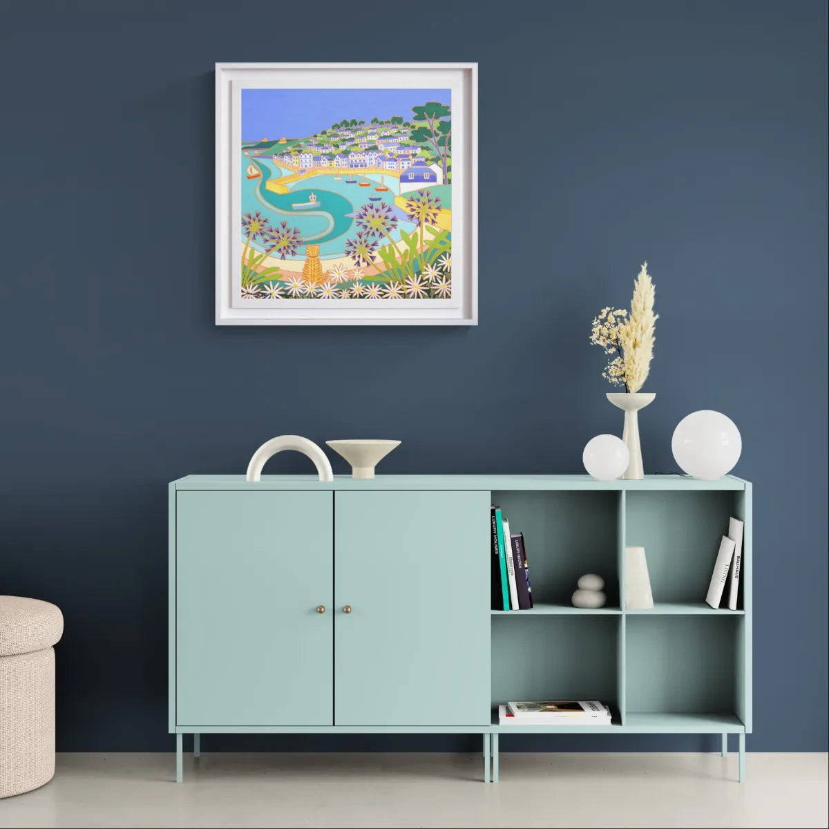 Light blue cabinet with decorative items against a dark blue wall with a framed artwork. 'Ginger Cat on the Wall, St Mawes’. 24x24 inches oil on canvas. Original Painting of Cornwall by Cornish Artist Joanne Short.