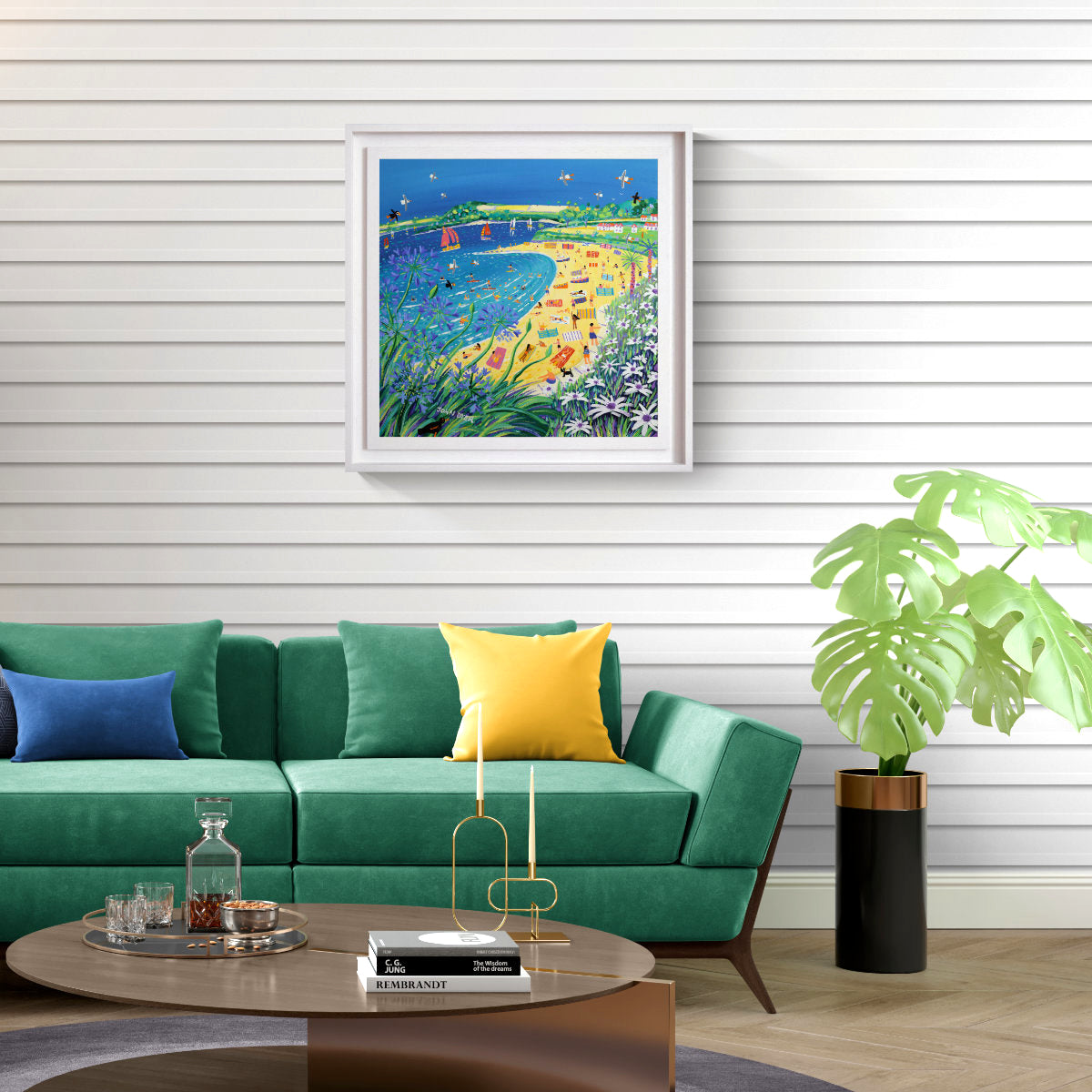 A colourful framed painting depicting a beach scene with a bridge and flowers, displayed on a white shiplap wall above a green sofa in a modern living room setting. 'High Summer, Gyllyngvase Beach, Falmouth', 24x24 inches acrylic on canvas. Original Painting by Cornish Artist John Dyer.