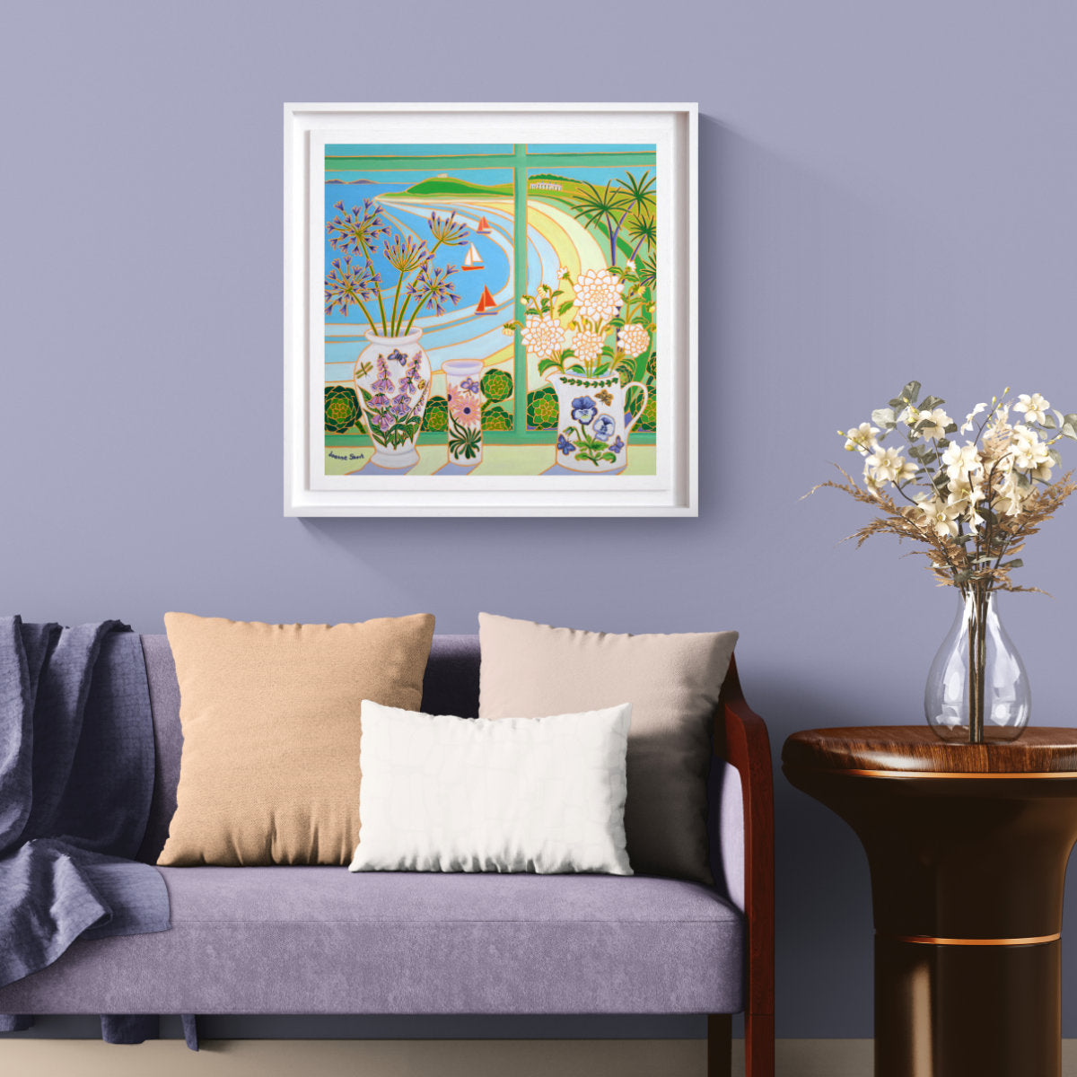A framed original oil painting depicting a colourful coastal landscape with flowers in vases and jugs  hangs on a lavender wall above a purple sofa with decorative pillows and a side table with dried flowers. Joanne Short Original Oil Painting of Cornwall. 'Flowers from the Garden, Old Grimsby, Tresco'. 24 x 24 inches oil on canvas.