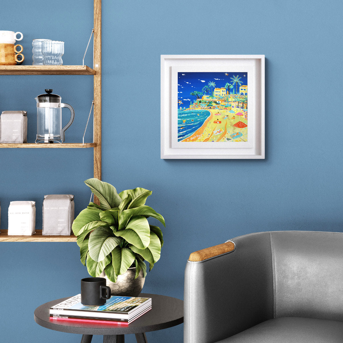 Living room with a blue wall, framed artwork, plant, and furniture. '‎⁨Summer Afternoon on Plage du Buse, Roquebrune-Cap-Martin⁩'. 12 x 12 inches acrylic on canvas. Painting of the South of France by John Dyer