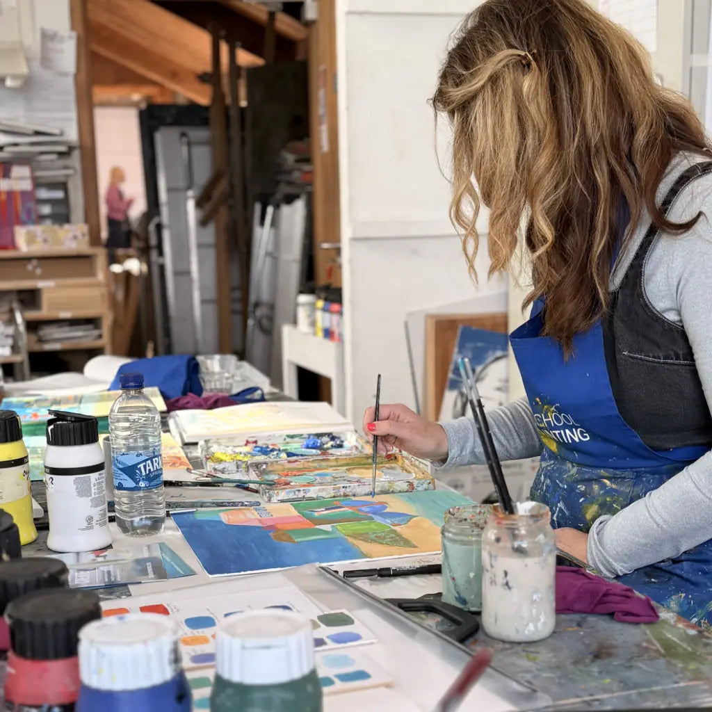 Person painting at a table with art supplies in a studio setting at the St Ives School of Painting during a John Dyer workshop