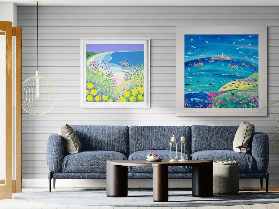 Two framed original painting artworks depicting coastal scenes with boats and landscapes on a modern plan grey coastal wall. Artists John Dyer and Joanne Short. Coastal interior setting.