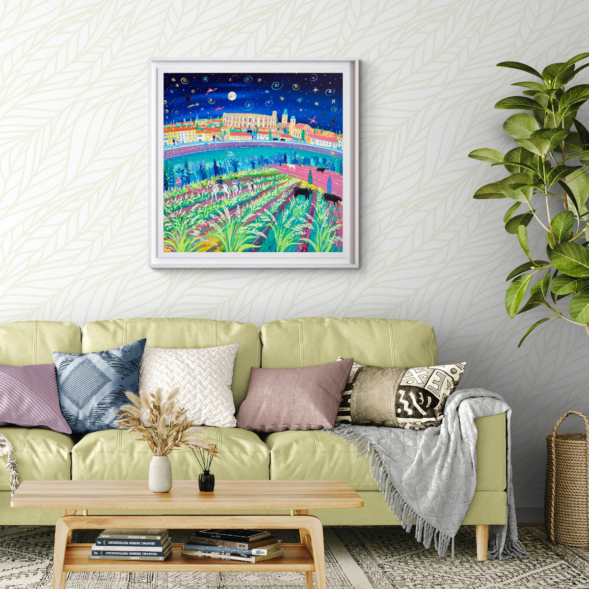 Colorful painting of a cityscape above a green sofa with decorative pillows in a living room. 'Rice Harvest Festival, Arles, Camargue'. 35.5 x 35.5 inches acrylic on canvas. Painting of Provence, France by John Dyer