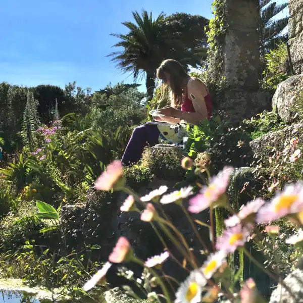 Cornish artist Joanne Short sitting in teh Tresco Abbey Gardens and painting teh flowers with plants and flowers in the foreground