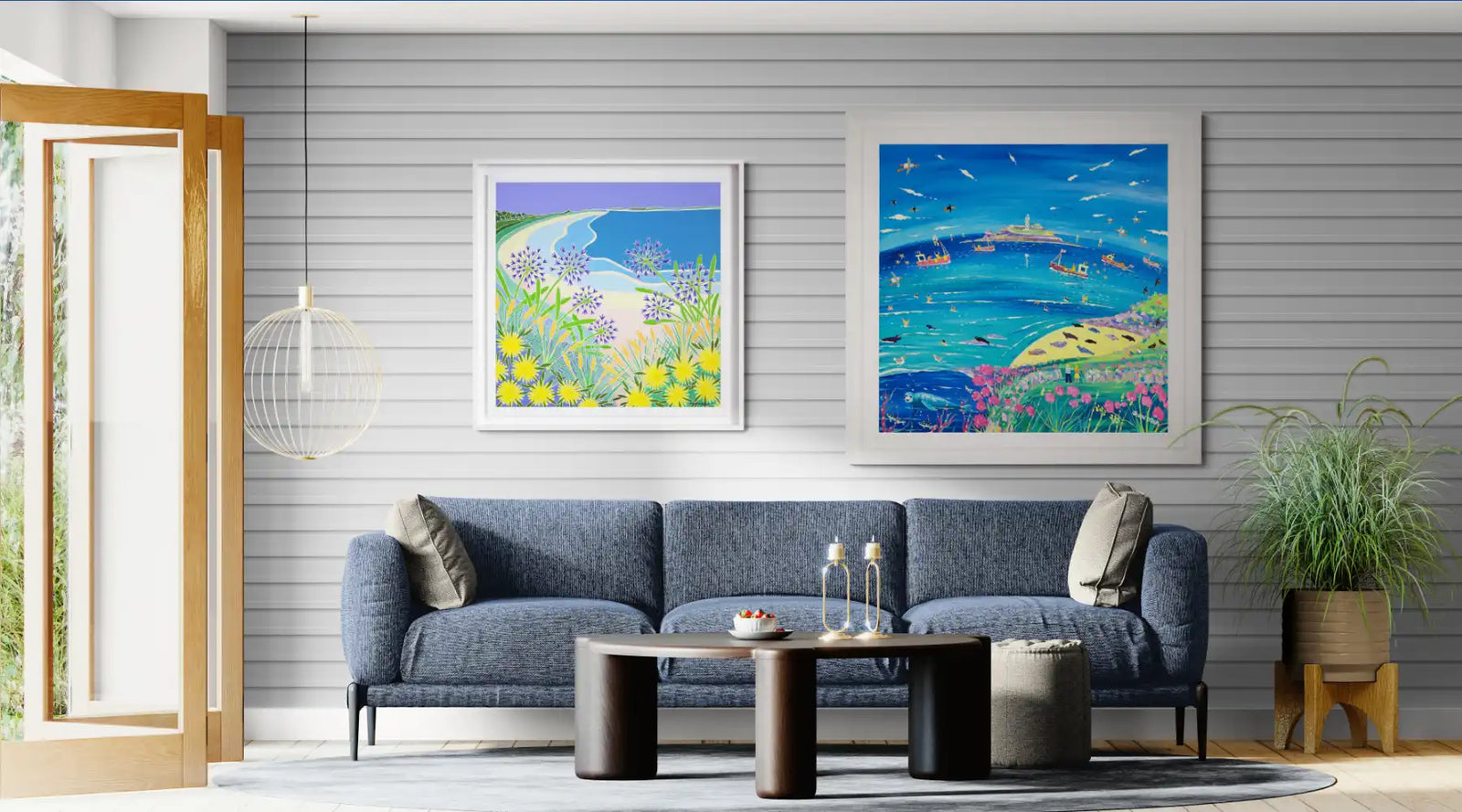 Living room with a grey sofa, coffee table, plant, and two colourful framed artworks by Cornish artists Joanne Short and John Dyer.
