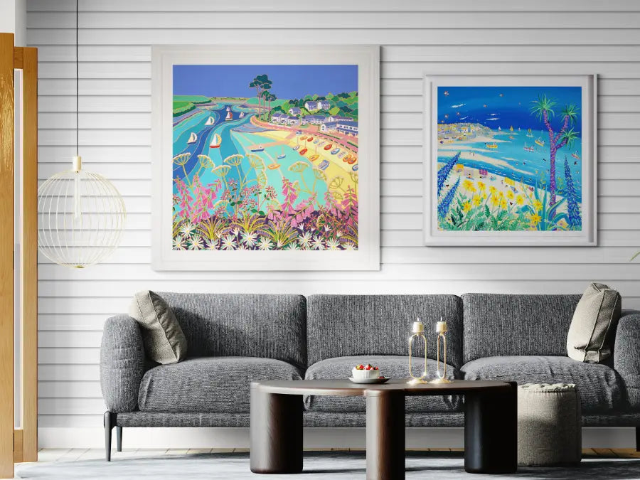 Living room with two colourful paintings of the Cornish coast by artist John Dyer and Joanne Short on a white wall above a grey sofa.