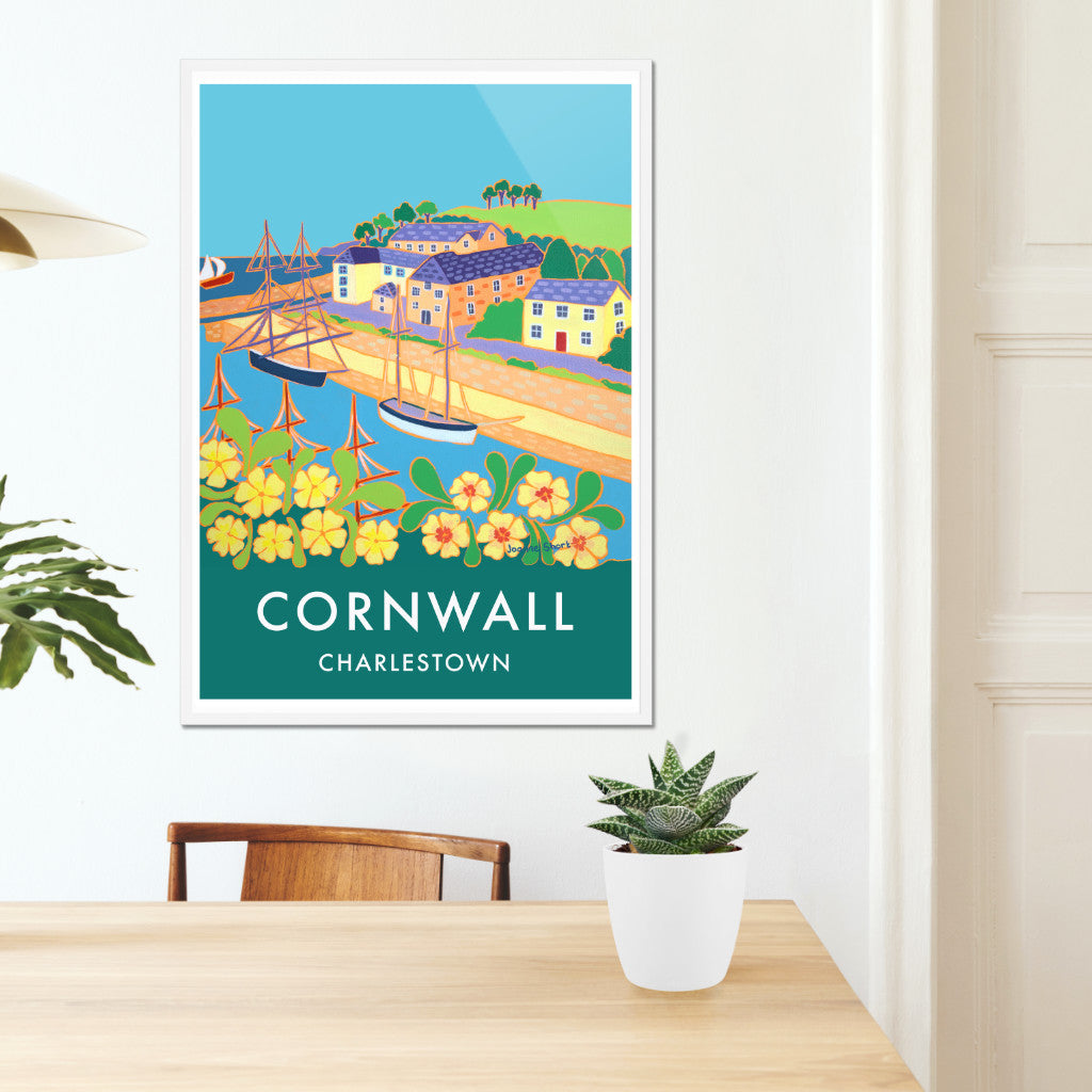 Cornwall framed wall art poster print of the harbour of Charlestown by Cornish artist Joanne Short. The Georgian working port of Charlestown in Cornwall, that is now often home to Tall Ships &amp; film crews such as Poldark &amp; Mansfield Park, has been painted for this vintage style travel poster by Cornish artist Joanne Short. Primroses jostle for space in the foreground. We look through the masts of a ship to the tall ships beyond that are waiting alongside the quay.