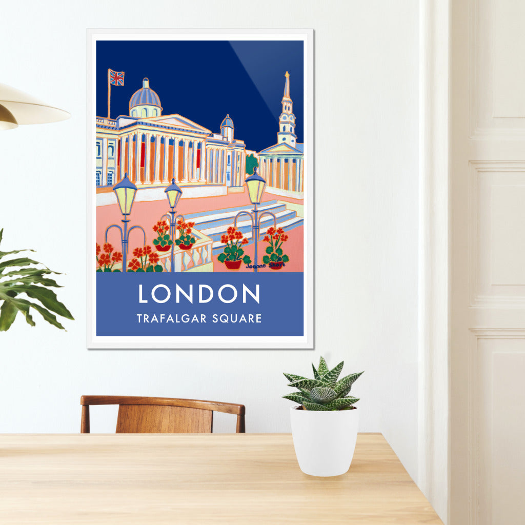 Framed London wall art poster print of Trafalgar Square and the National Gallery by British artist Joanne Short. A stunning vintage style travel poster featuring Joanne Short&#39;s painting &#39;Blue Sky, Trafalgar Square&#39;. A union jack flag flutters above the National Gallery set against a midnight blue sky. The church of St Martin-in-the-Fields also features in the poster set back beyond the classic London street lights. Red geraniums complete this delightful composition.